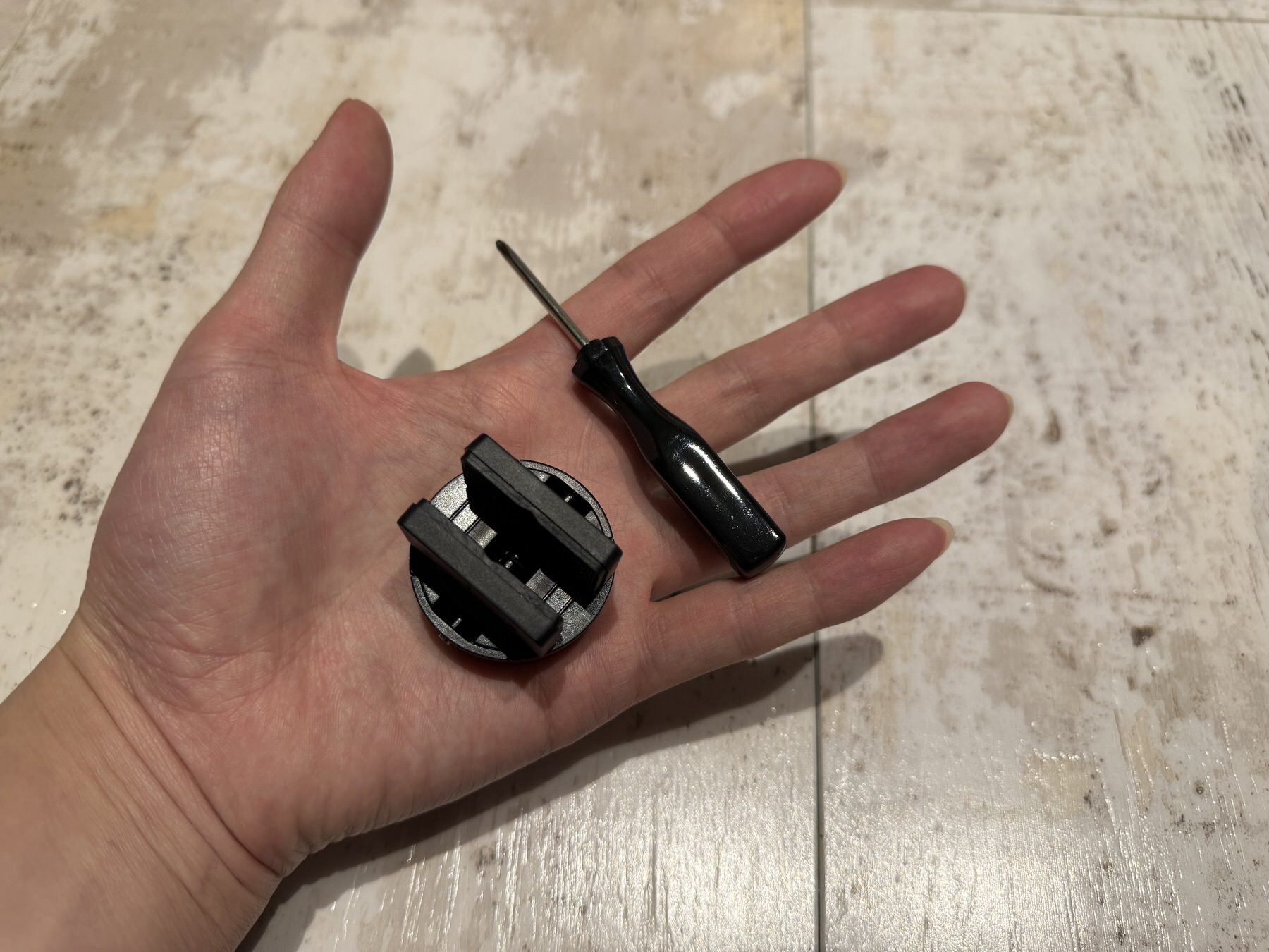 SwitchBot ロックProのサムターンアダプターと付属ドライバーを手のひらに載せた様子